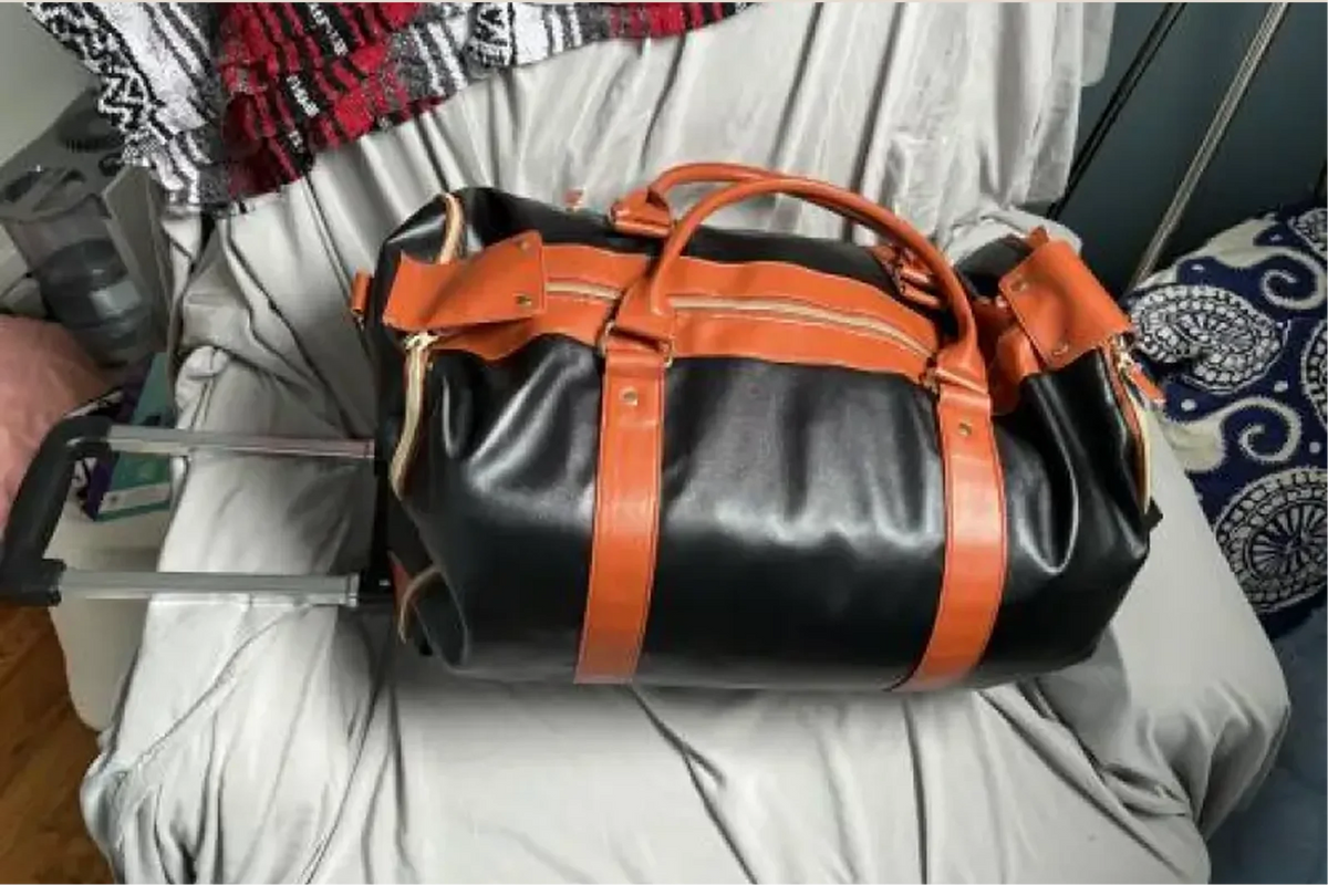 A black and tan Vohxe bag with its wheels attached, resting on a bed