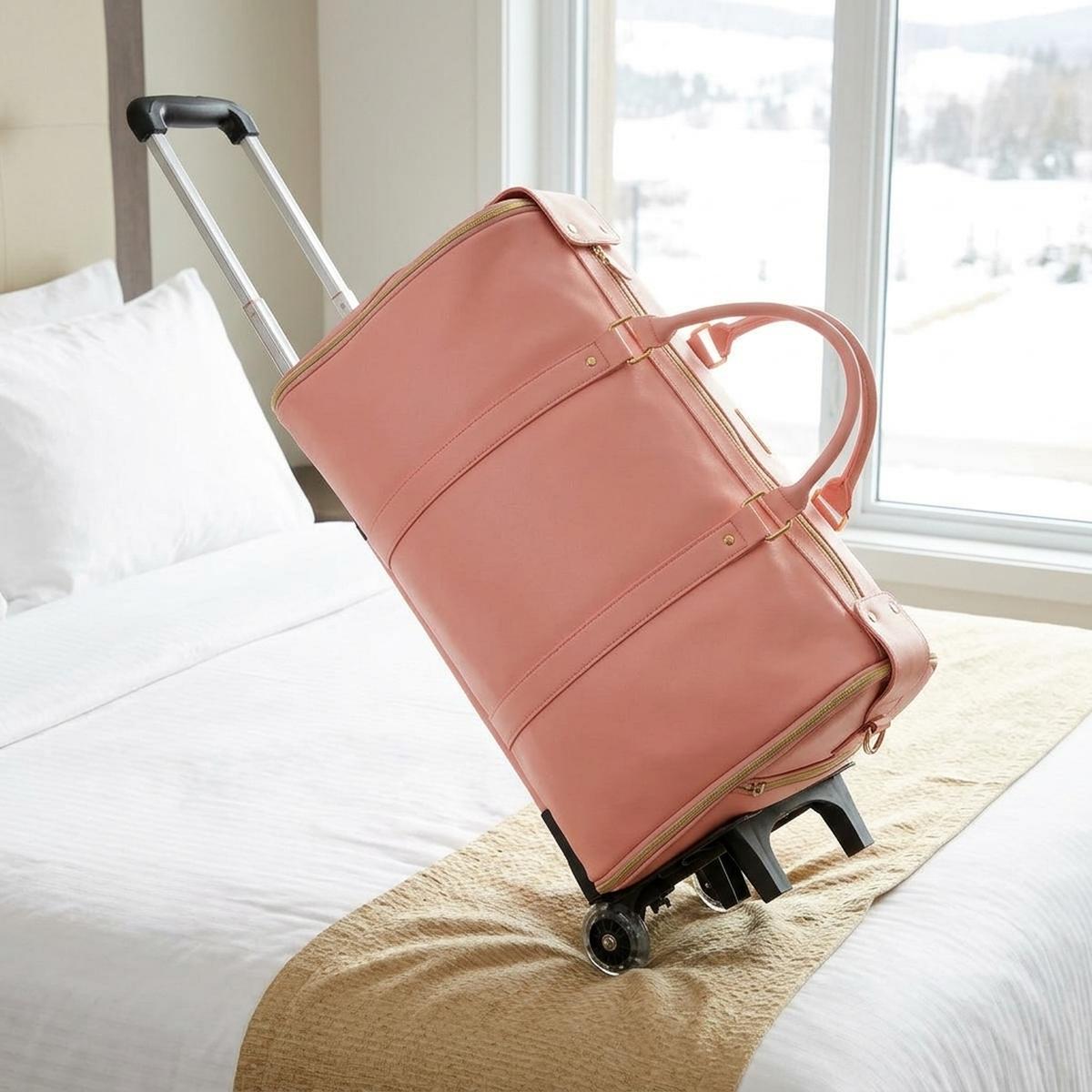 The rose pink Vohxe Travel Bag 2.0 packed and zipped on a hotel bed
