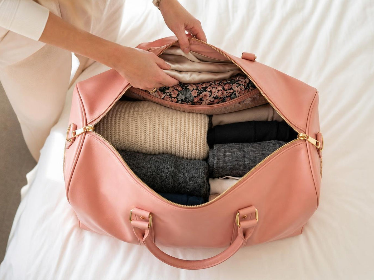 The rose pink travel bag open on a bed, dresses hanging flat in the garment compartment and everything else compressed neatly below